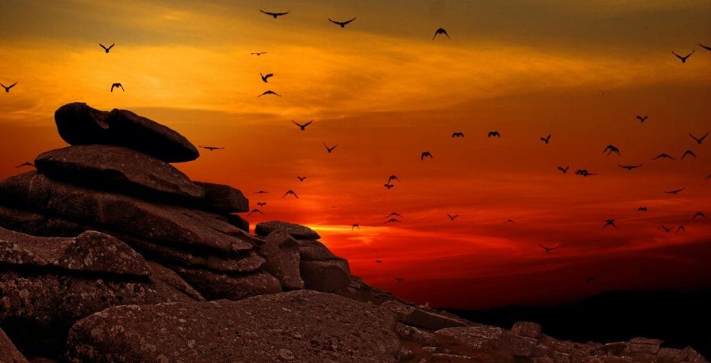 Silhouetted birds flying over rocky formation during a vibrant sunset, capturing nature's serene beauty.